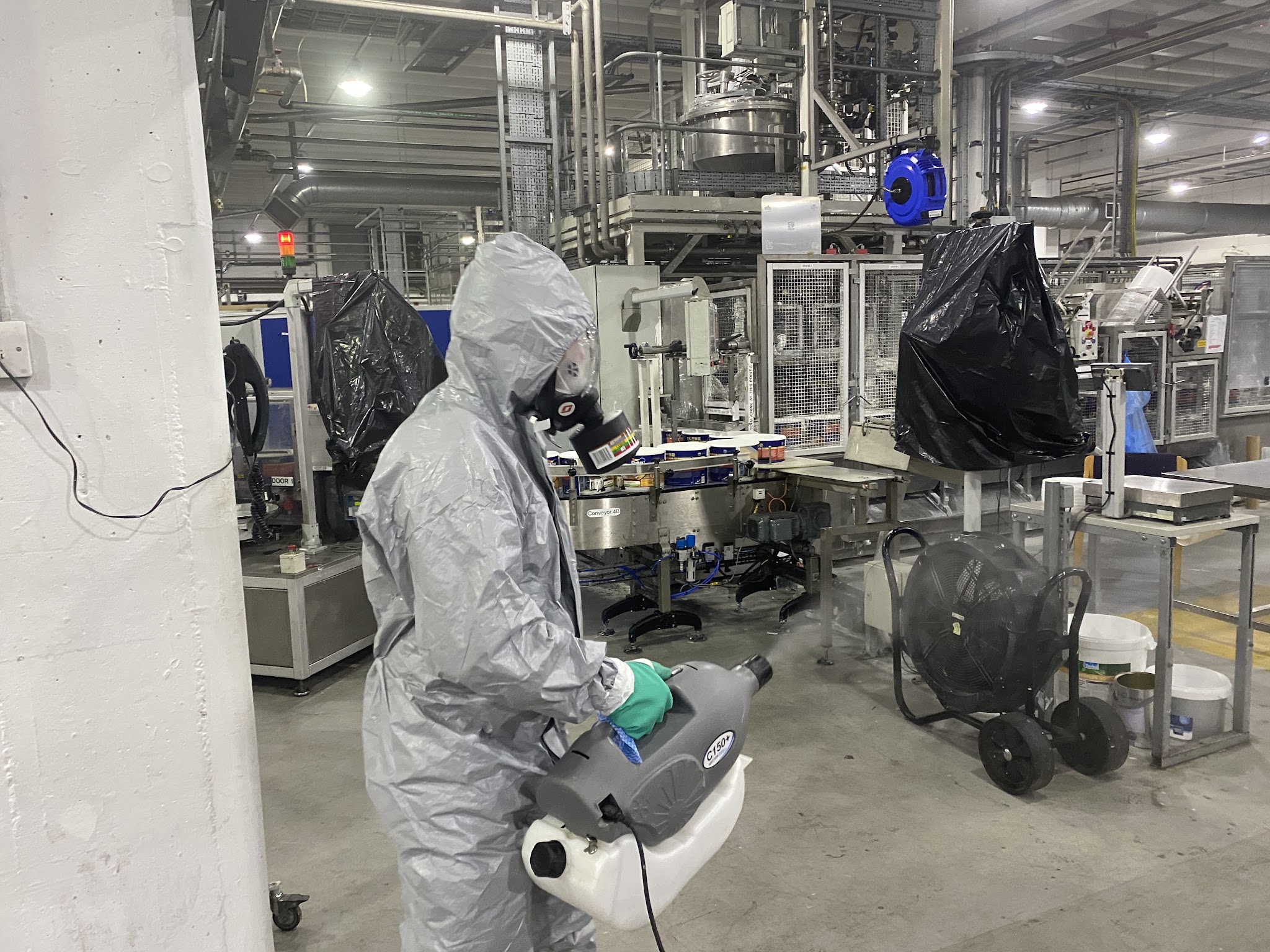 An EBC operative in a full protective suit and respirator treating a factory floor with a fogger